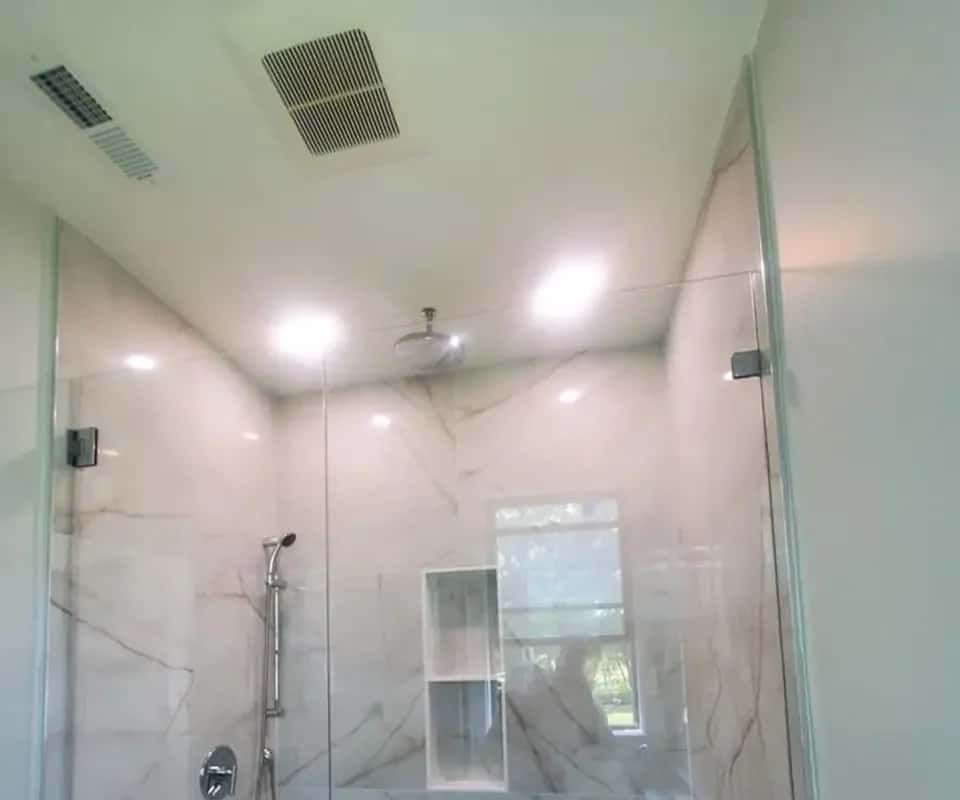 Walk-in shower with large marble-look wall tile, a frameless glass panel, a built-in niche and a window (Massachusetts)