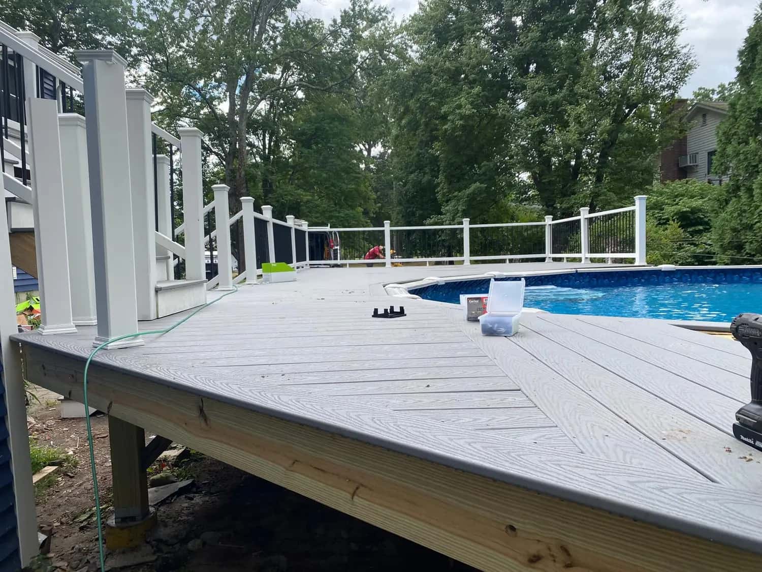 Deck with gray decking, a contrasting border and white railings wrapped around an above-ground pool, on a pressure-treated frame