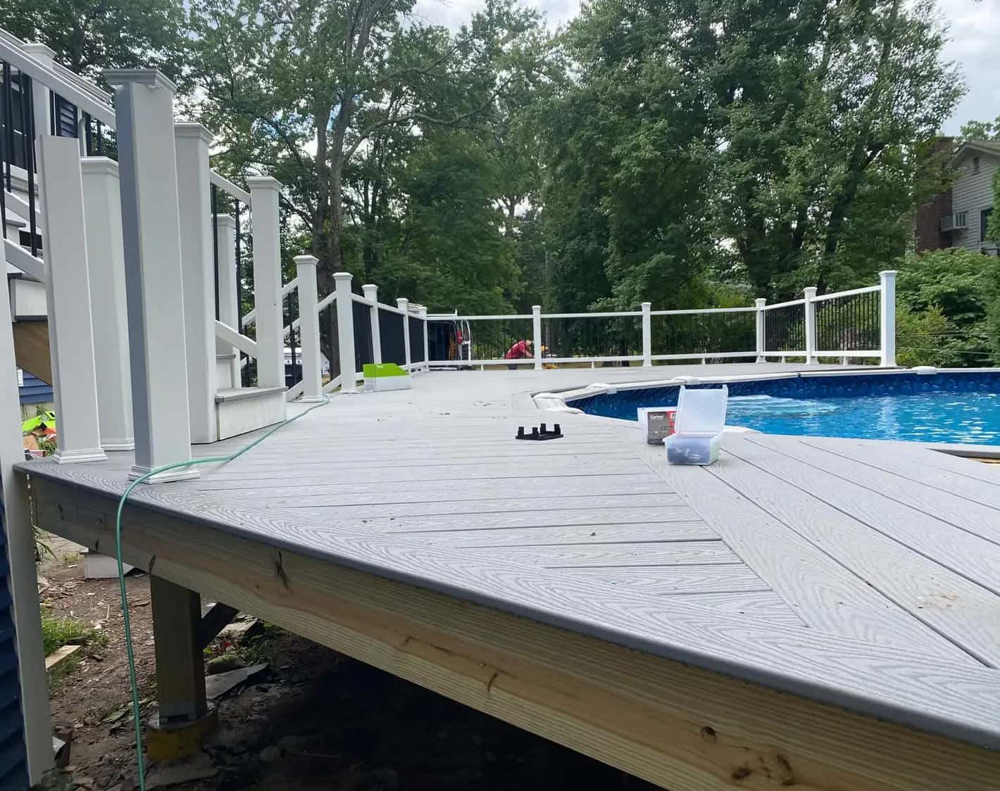 Composite deck with white railings built around an above-ground pool by Waterfront Construction in Salem, NH