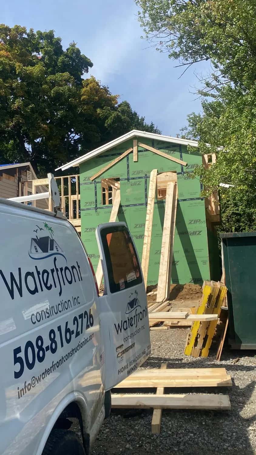 Waterfront Construction Inc work van parked at a home-addition job in Lynnfield, MA, with the new addition framed and sheathed behind it