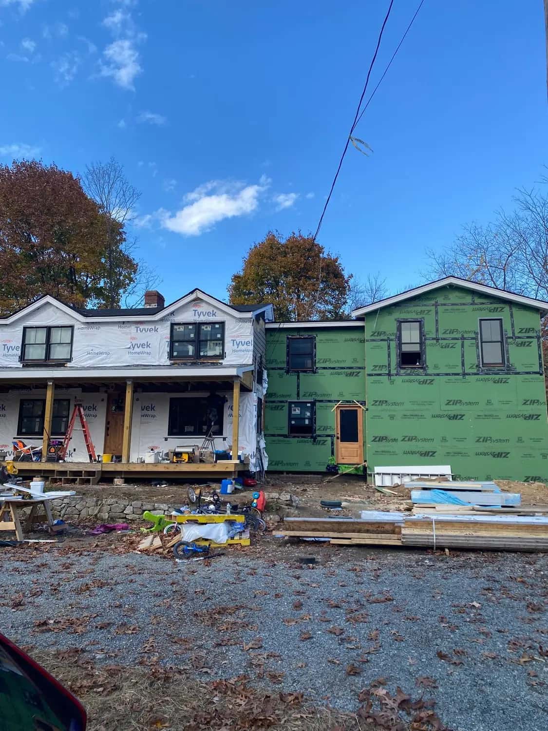 Main house in white house wrap beside a two-story addition sheathed in green panels with taped seams