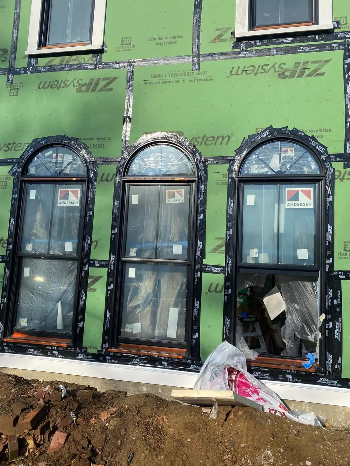 Three new arched windows with factory labels still on, set into green sheathing with taped seams