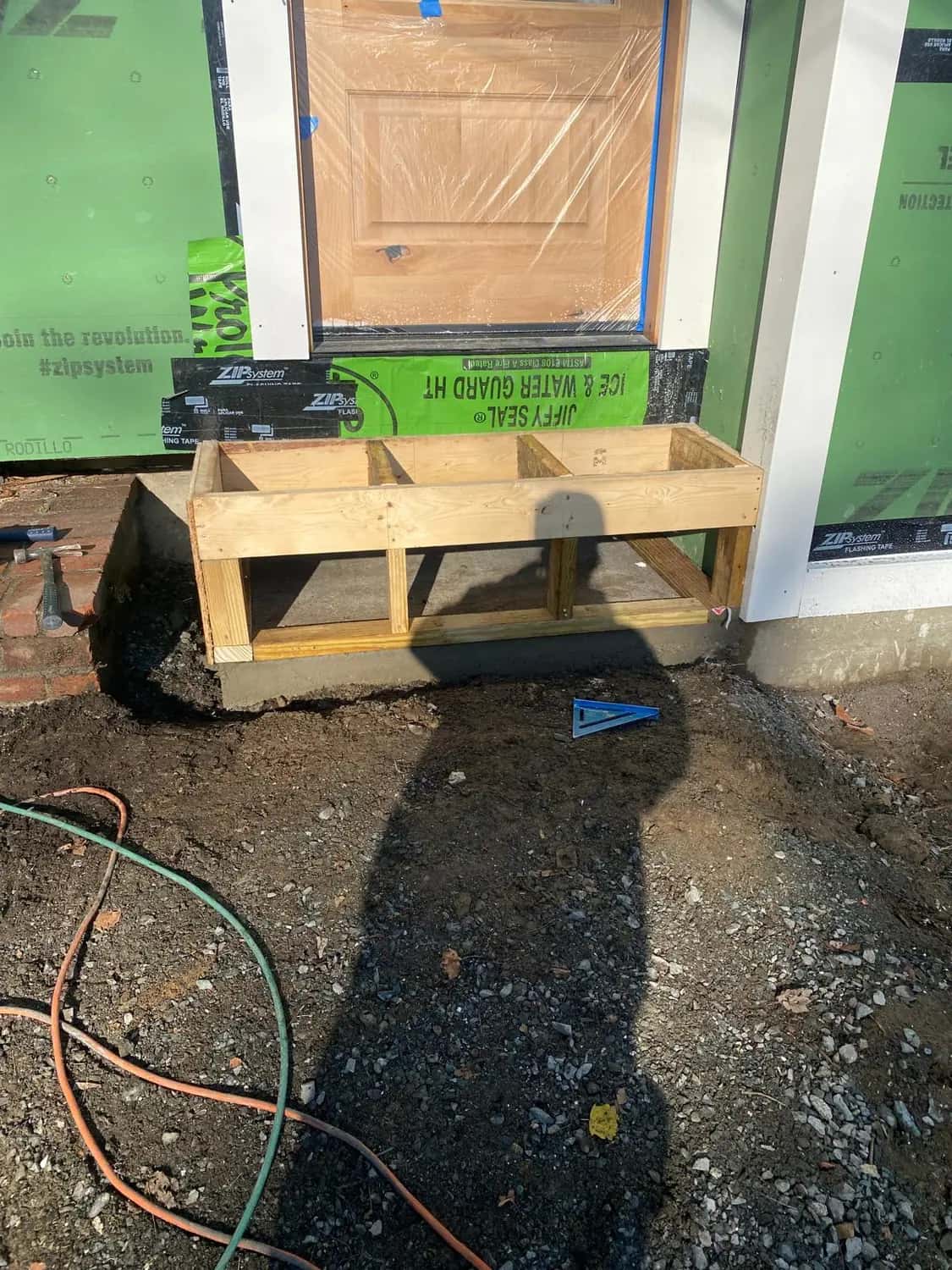New entry door in protective plastic, with flashing membrane at the sill and a wooden form for a concrete step