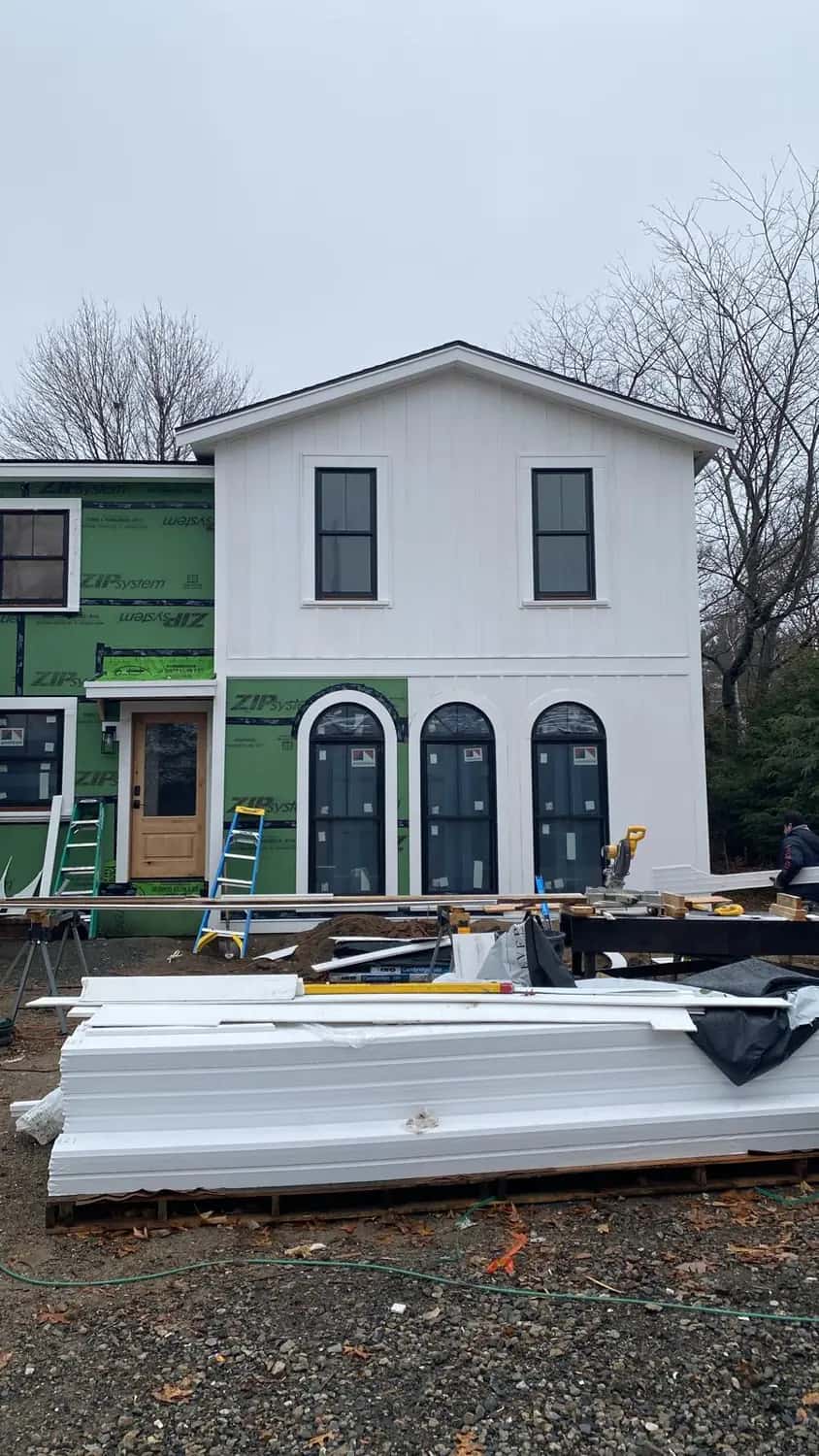 Two-story addition with new white vertical siding on the upper story, three arched windows and bundles of siding staged in the yard