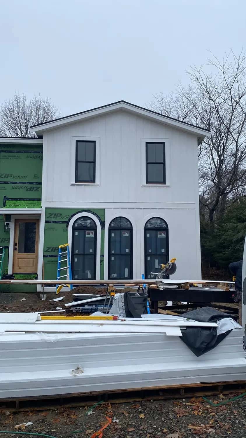 White vertical siding nearly finished around three arched windows and a new entry door on a home addition (Lynnfield, MA)