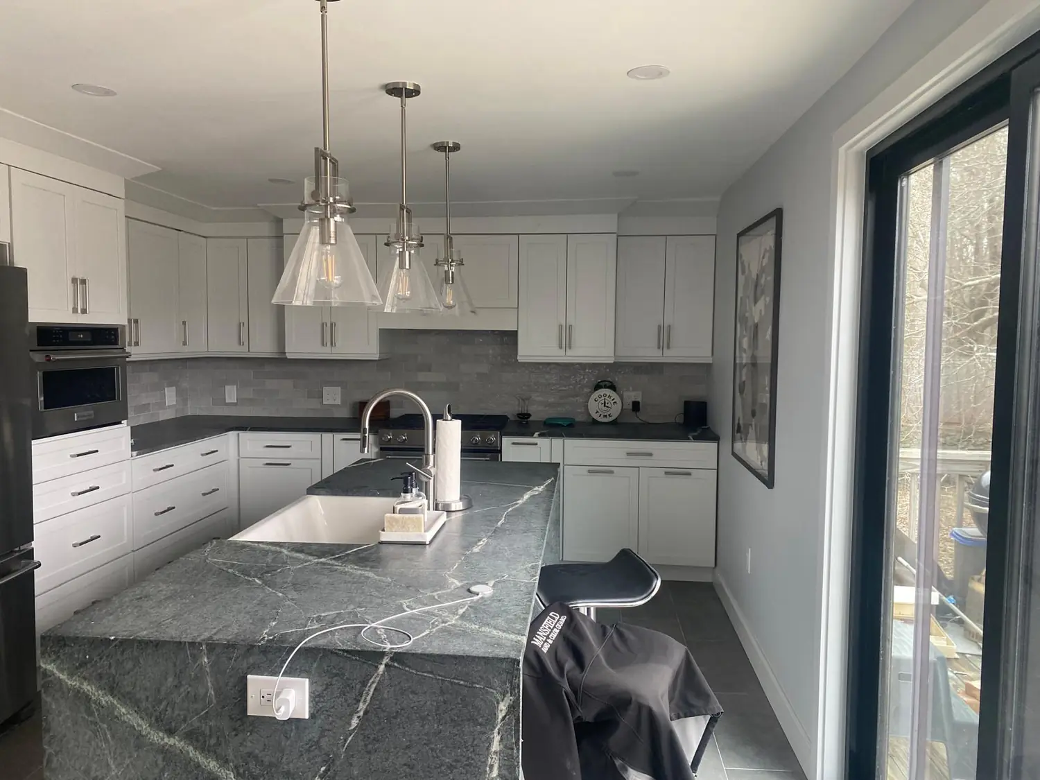 Kitchen island with a dark veined stone-look countertop and waterfall edge, white cabinets and a sliding door (Mansfield, MA)
